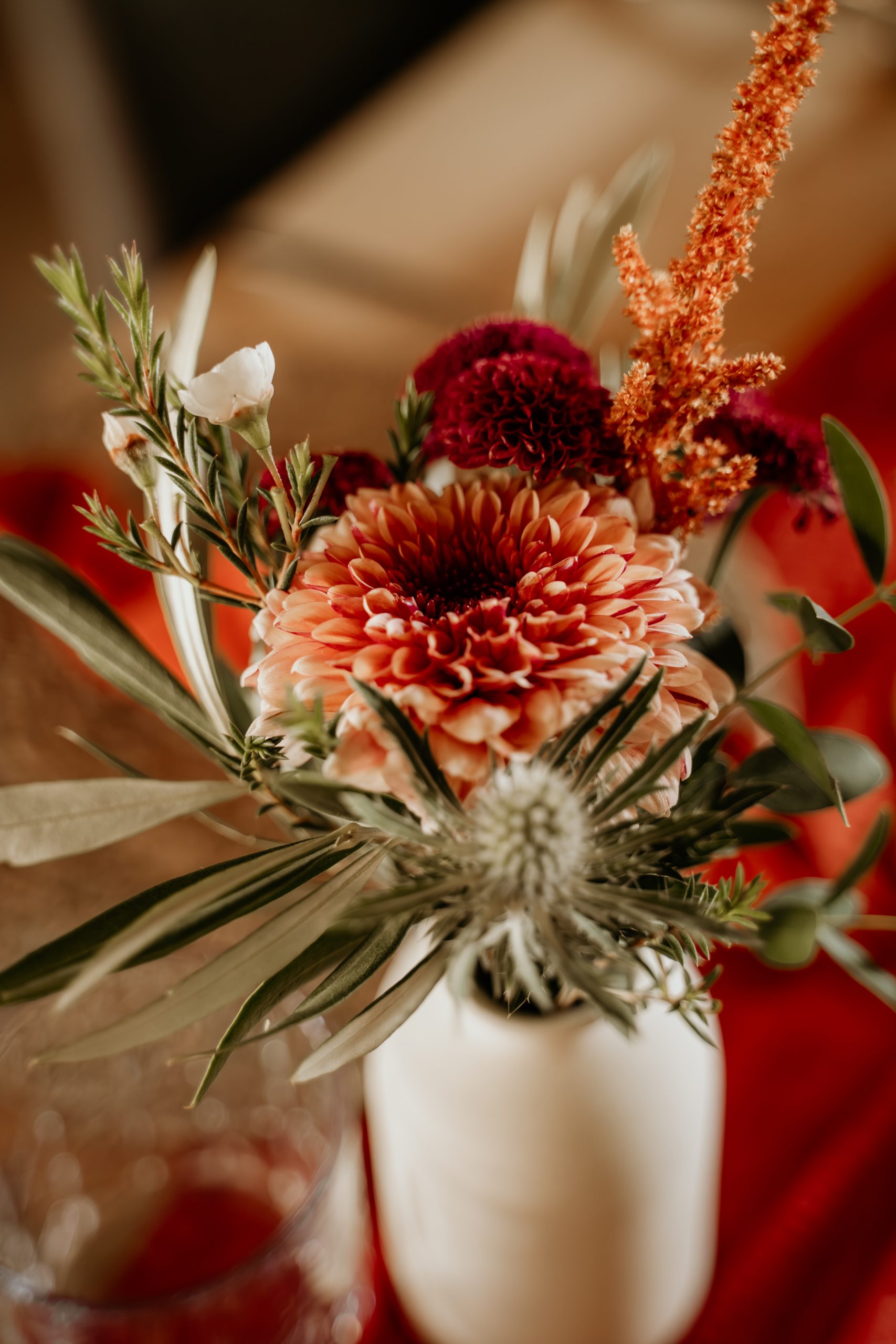 Nahaufnahme: Blumengesteck mit Chrysantheme, Distel und Amaranth in weißer Vase